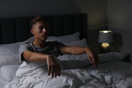 Young man suffering from sleepwalking on bed at homeの写真素材