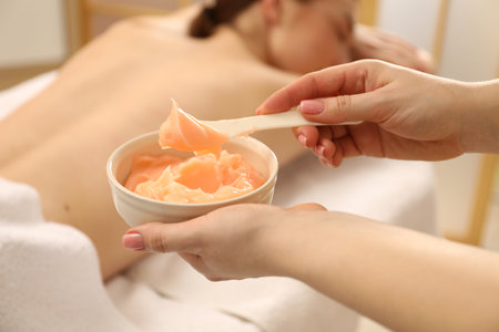 Esthetician applying cosmetic product for body wraps treatment onto woman's back in spa salon, closeupの写真素材