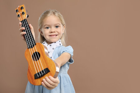 Little girl with ukulele on brown backgroundの写真素材