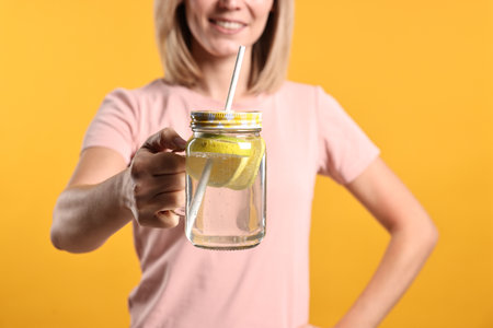 Woman with glass of lemonade on orange background, closeup. Refreshing drinkの写真素材