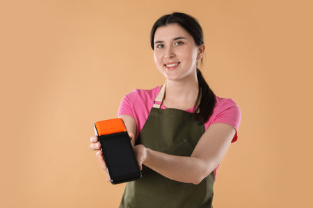 Happy young woman in apron with payment terminal on beige backgroundの写真素材