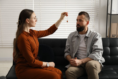 Psychologist using pendulum while working with patient during hypnosis session indoorsの写真素材