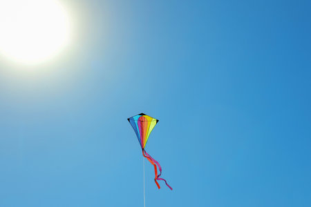 One colorful kite flying in blue sky on sunny day.