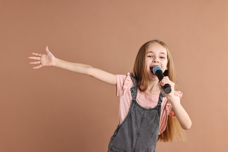 Little girl with microphone singing on light brown backgroundの写真素材
