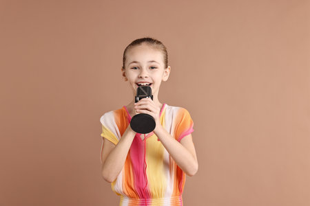 Little girl with microphone on light brown backgroundの写真素材