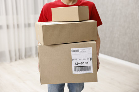 Man holding parcels with shipping labels indoors, closeup