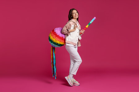 Happy woman with colorful pinata and stick on pink backgroundの写真素材