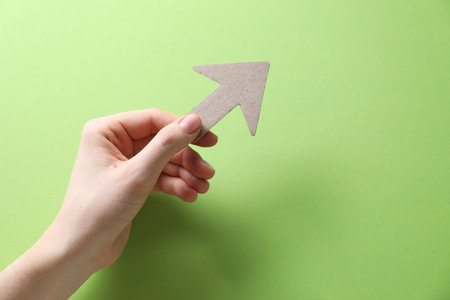 Woman with paper arrow on light green background, top view. Space for textの写真素材