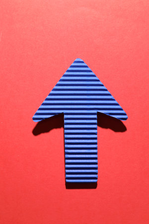 One blue paper arrow on red background, top viewの写真素材