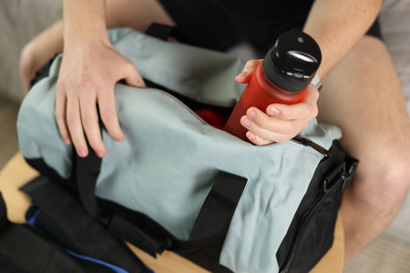 Man putting bottle of water into gym bag indoors, closeupの写真素材