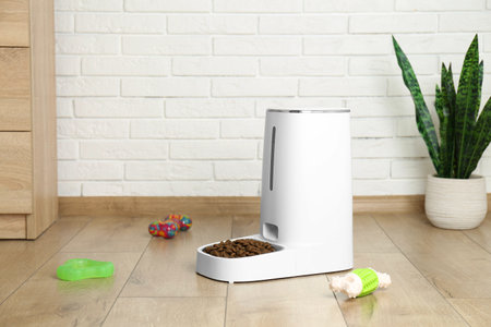 Dry pet food in automatic feeder and toys on floor indoorsの写真素材