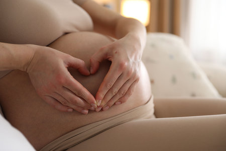 Pregnant woman making heart with hands on her belly at home, closeupの写真素材