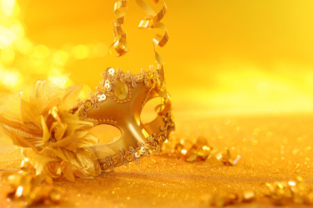 Beautiful carnival mask on golden shiny surface, closeup. Space for textの写真素材