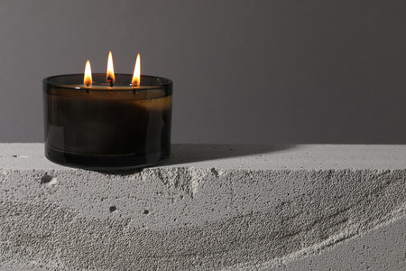 Burning soy wax candle on concrete block against gray background, space for textの写真素材
