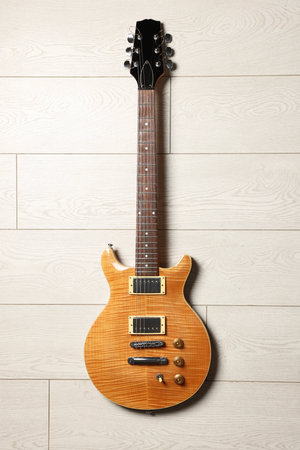 One modern electric guitar on light wooden background, top view