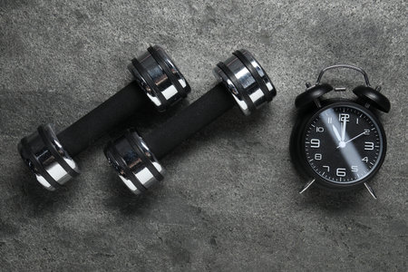 Alarm clock and dumbbells on gray background, flat layの写真素材