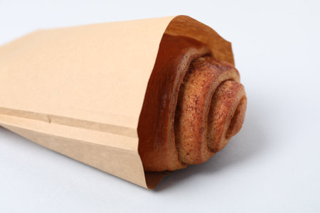 Paper bag with freshly baked bun on white background, closeup