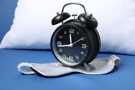 Alarm clock, sleep mask and pillow on blue background. Time for sleeping