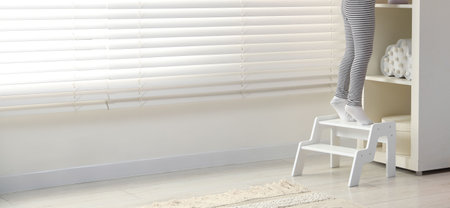 Little girl standing on step stool indoors, closeup. Space for text
