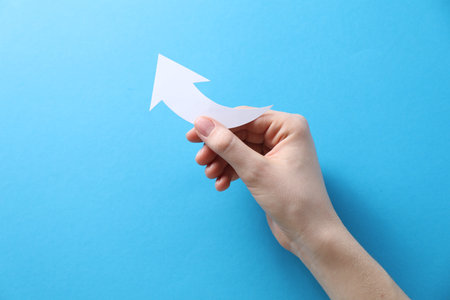 Woman with paper arrow on light blue background, top view. Space for textの写真素材