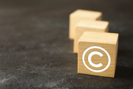 Wooden cube with copyright symbol on gray textured table, closeup. Space for text