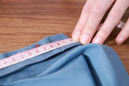 Woman with measuring tape and blue shirt working at wooden table, closeup