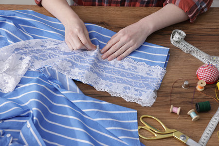 Woman sewing shirt with thread at wooden table, top view