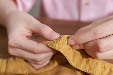 Woman sewing shirt with needle at table indoors, closeupの写真素材