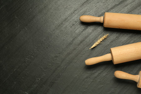 Wooden rolling pins and spike on dark gray textured table, flat lay. Space for text