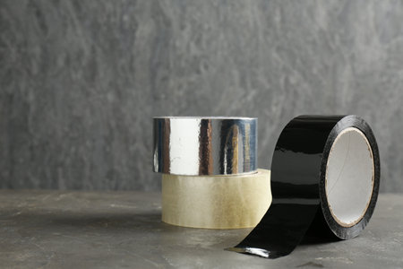 Rolls of different adhesive tapes on grey table, space for text