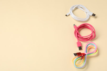 USB charge cables on beige background, above view. Space for text