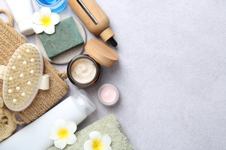 Different body care products and plumeria flowers on light grey table, flat lay. Space for text