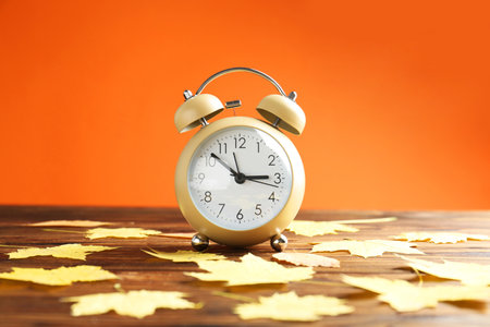 Autumn time. Alarm clock and golden leaves on wooden table