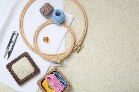 Embroidery. Different sewing accessories on beige textured table, flat lay. Space for text