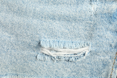 Texture of ripped light blue jeans as background, top view