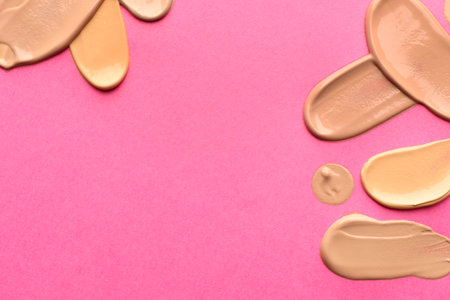 Foundation on pink background, top view with space for text. Smears of cosmetic product