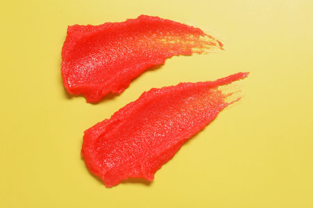 Samples of body scrub on yellow background, top view