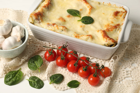 Delicious spinach lasagna in baking dish and ingredients on white tableの写真素材