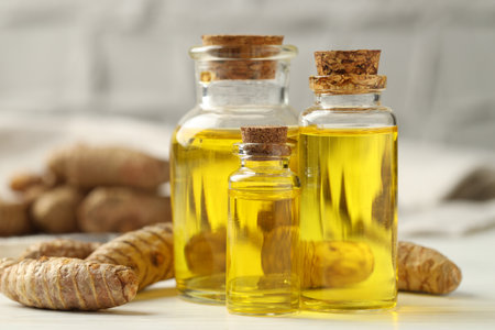 Tumeric oil and roots on white table, closeupの写真素材