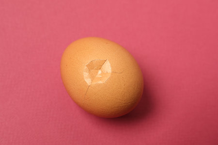One egg with cracked shell on pink background, closeupの写真素材