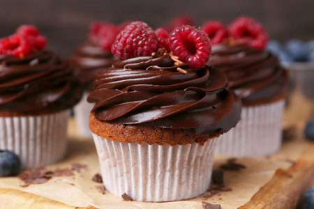 Tasty cupcakes with chocolate cream and raspberries on wooden board, closeup