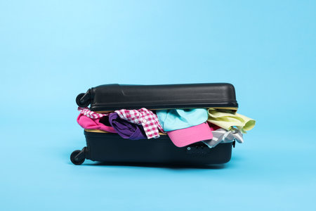 Packed suitcase full of clothes on light blue backgroundの写真素材