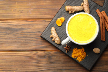 Tasty turmeric latte in cup and spices on wooden table, flat lay. Space for textの写真素材