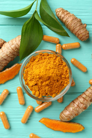 Turmeric capsules, roots, powder and green leaves on turquoise wooden table, flat layの写真素材