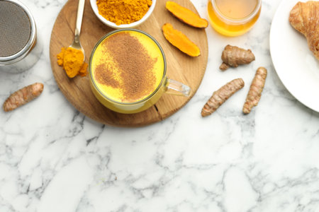 Turmeric latte, powder and rhizomes on white marble table, flat lay. Space for text