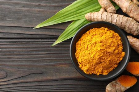 Aromatic turmeric powder in bowl, fresh roots and leaves on wooden table, flat lay. Space for textの写真素材