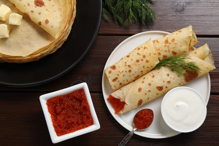 Crepes with red caviar served on wooden table, flat lay