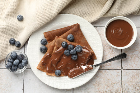 Delicious chocolate crepes with sweet paste and blueberries on light tiled table, flat layの写真素材