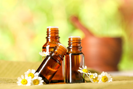 Bottles of essential oil and chamomile flowers on cloth, closeupの写真素材