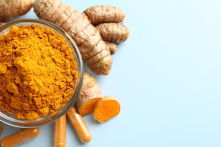 Turmeric capsules, powder and roots on light blue background, flat lay. Space for text